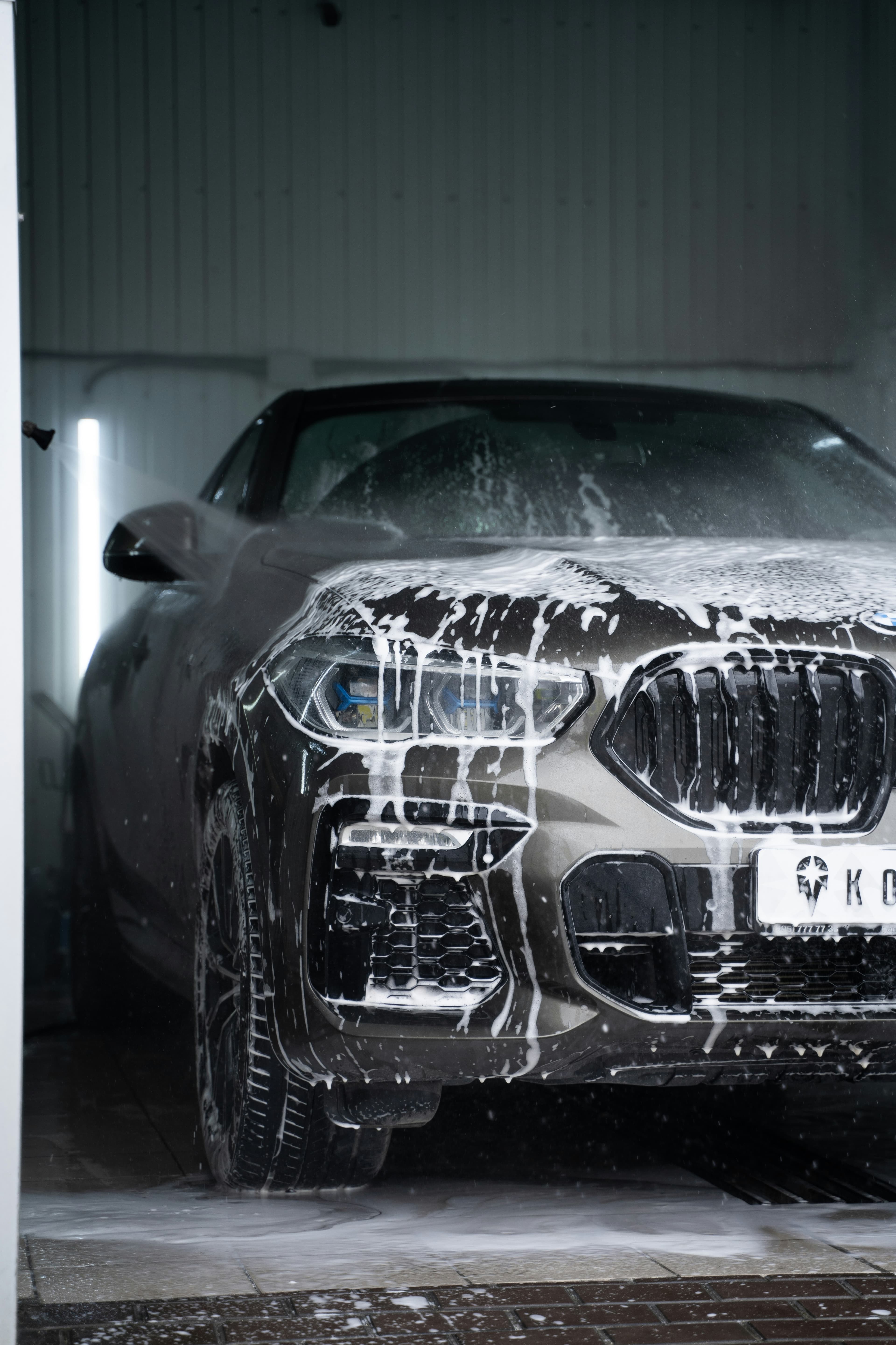 Dark grey BMW SUV covered in white soap foam during a professional car wash.